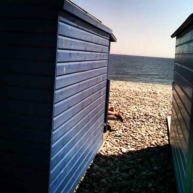 A sunbather's feet glimpsed in the gap between two beach huts