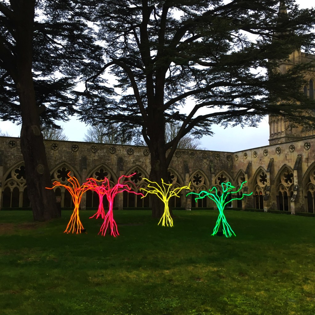 Luminous wire sculptures below the ancient yew on the lawn of a cathedral cloisters