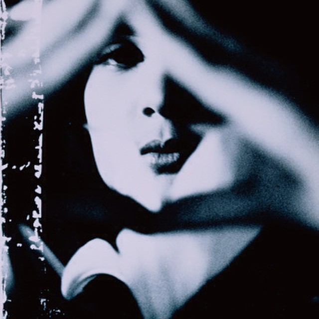 A black and white photo of a woman looking at the camera through the roof of her fingers. 