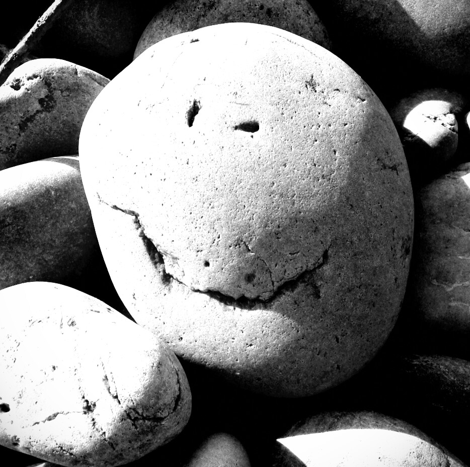A pebble on a beach with the appearance of a smiling face in its cracks and holes
