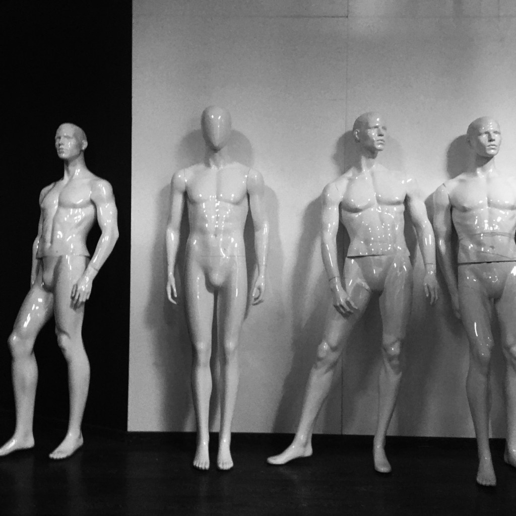 Four disused mannequinns stand in a line against the bare wall of a closed down shop