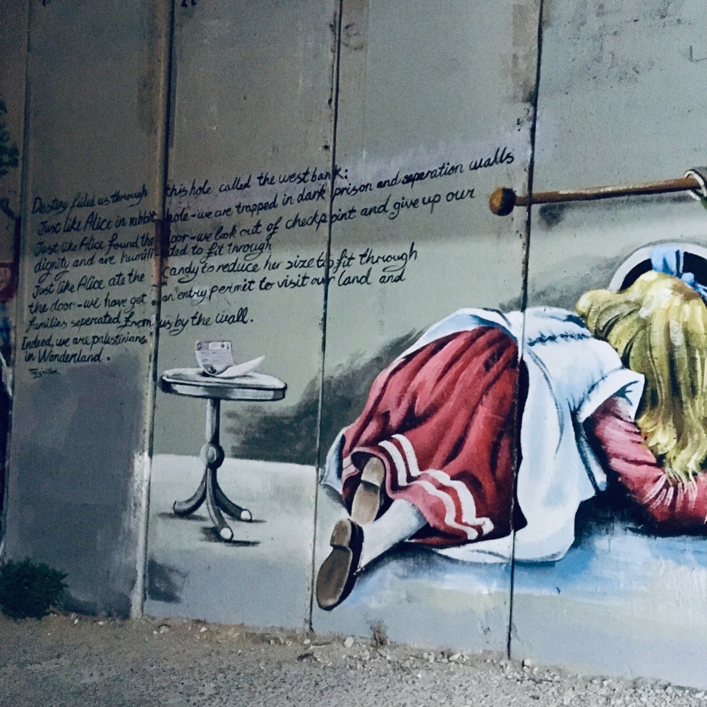 A drawing of Alice in Wonderland crawling through the concrete wall at Bethlehem, next to text describing the impact of checkpoints in the daily lives of Palestinians