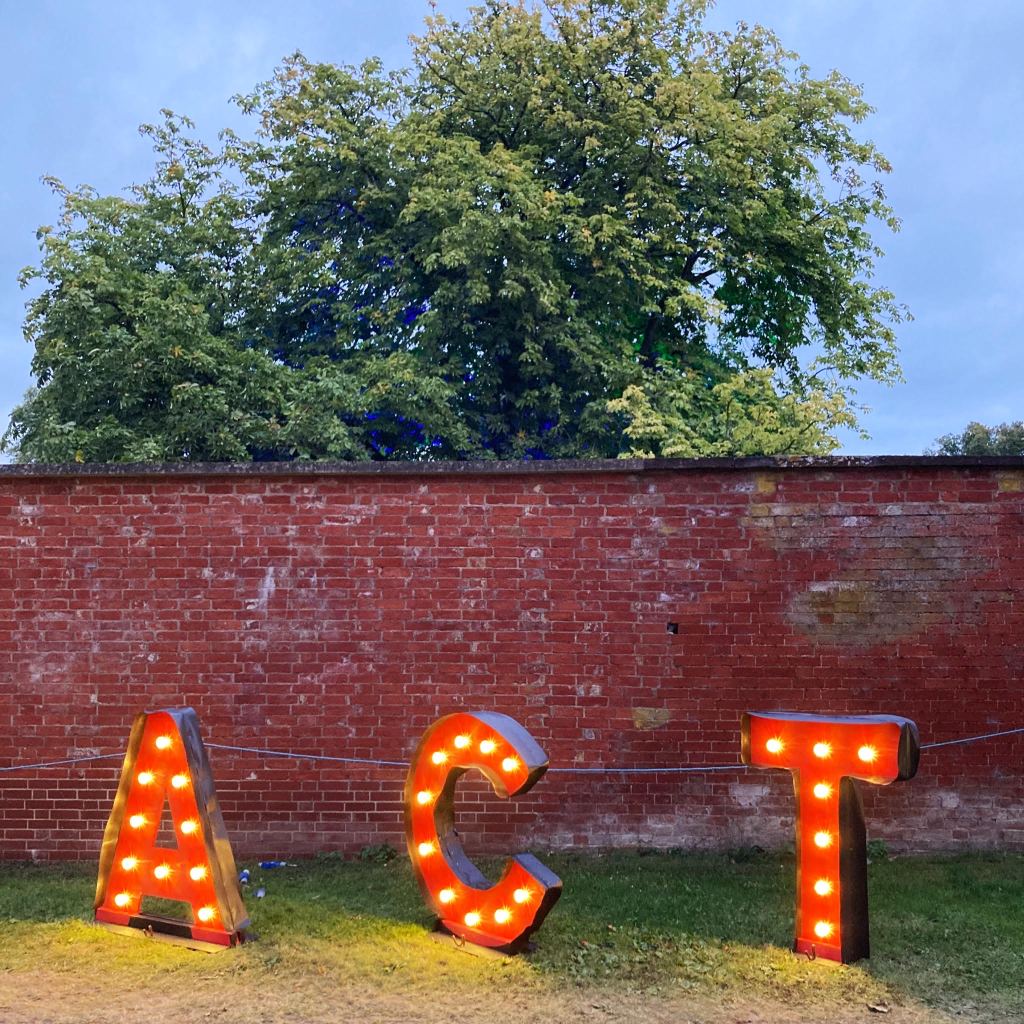 One metre tall red letters A - C - T, illumined by white lightbulbs, stand in front of an ancient red brick wall.