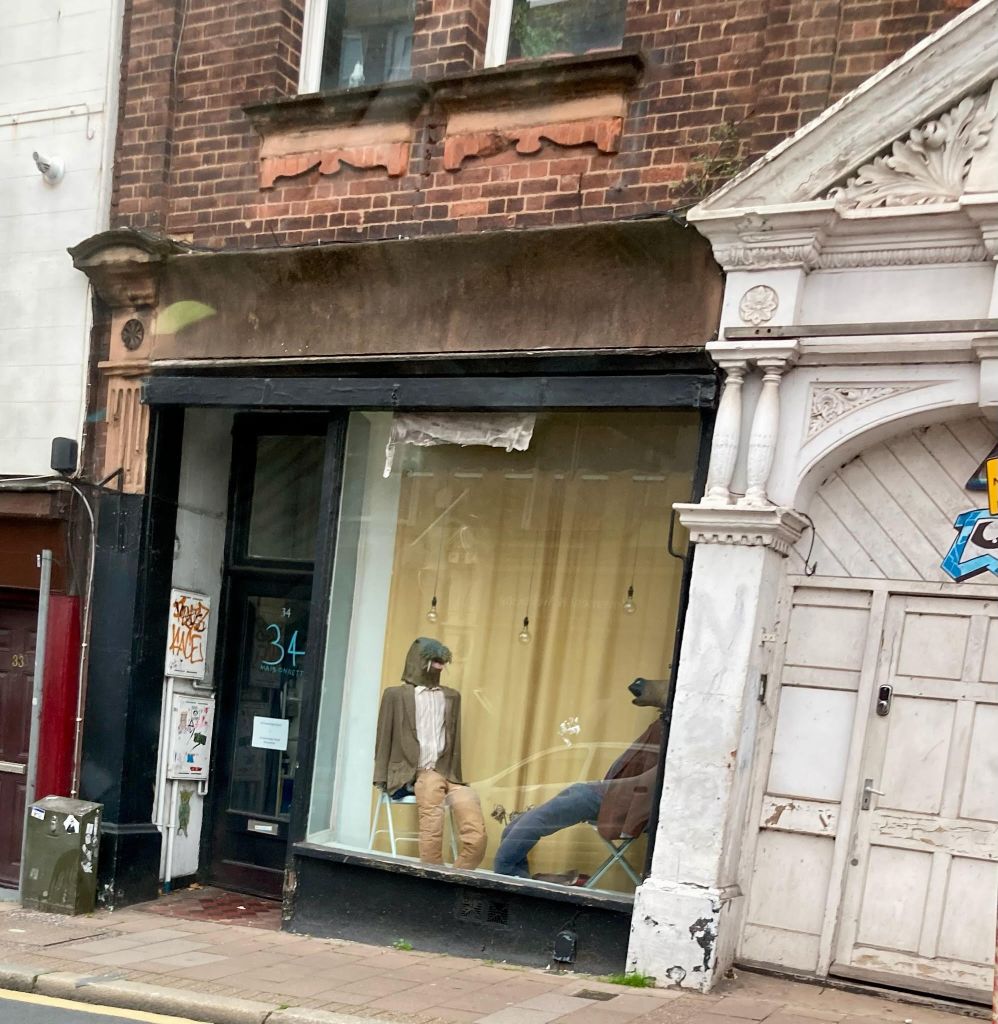 A shop window in Exeter featuring two figures dressed in old clothes, one wearing a walrus mask, the other a horse's head.