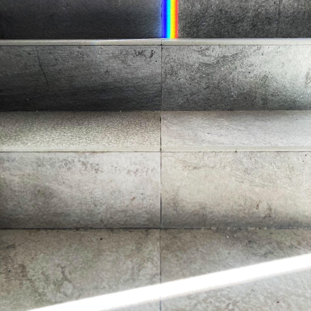 A beam of light falls across grey stone steps, making a rainbow prism on the top step.