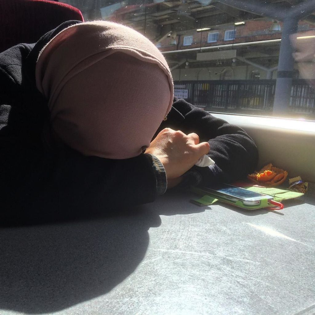 A woman wearing a head covering rests her head on her hands on a train table.