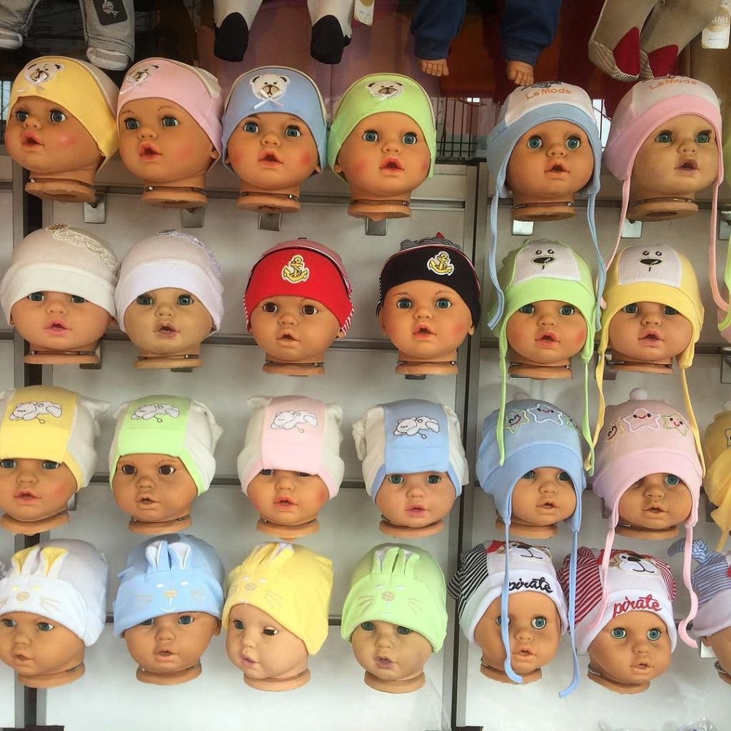 Rows of identical dummies of the heads of babies in a shop window, each wearing a different coloured hat.