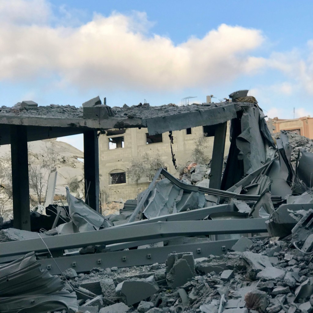 Twisted metal and rubble frame the outline of a bombed house,