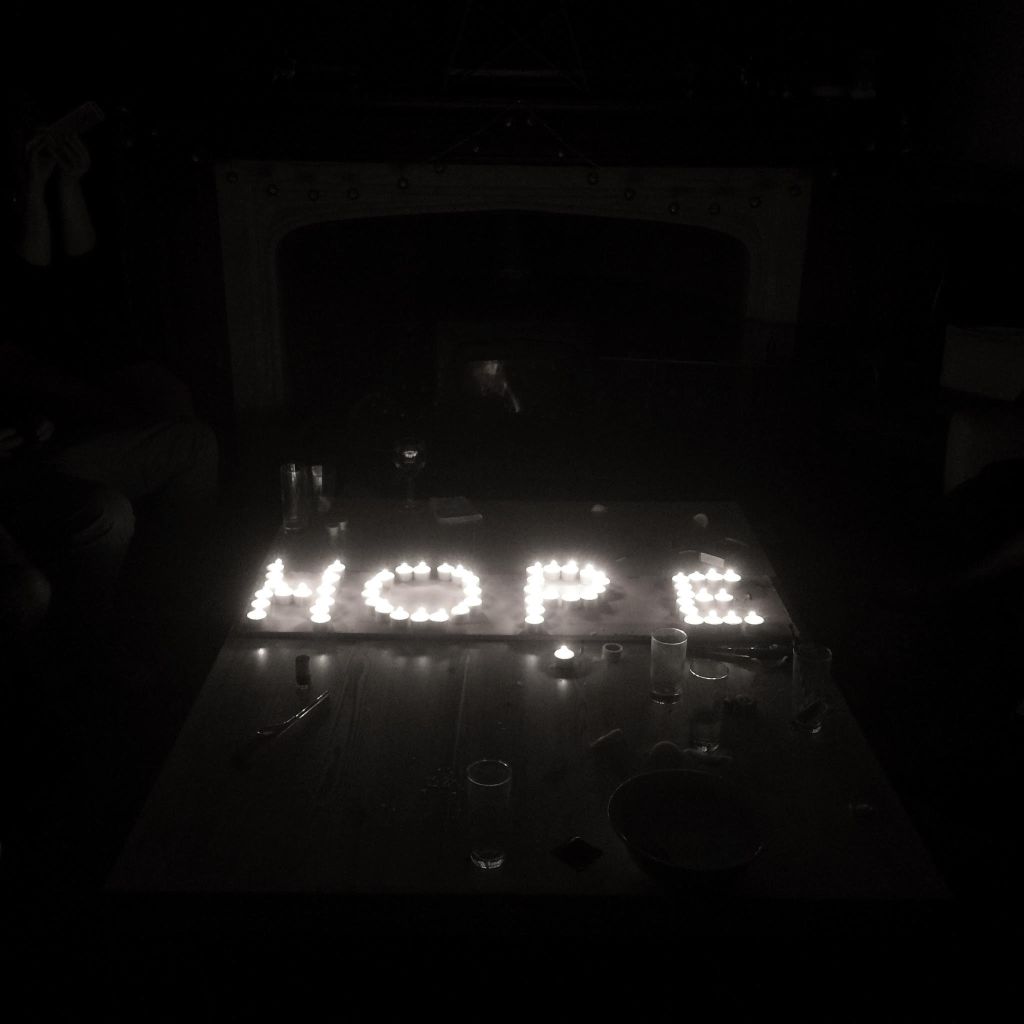 Tea lights on a table top spelling out the word 'HOPE' in a darkened room, surrounded by empty glasses.