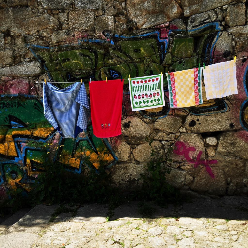 Brightly coloured washing on a line, in front of graffiti on ancient city walls.