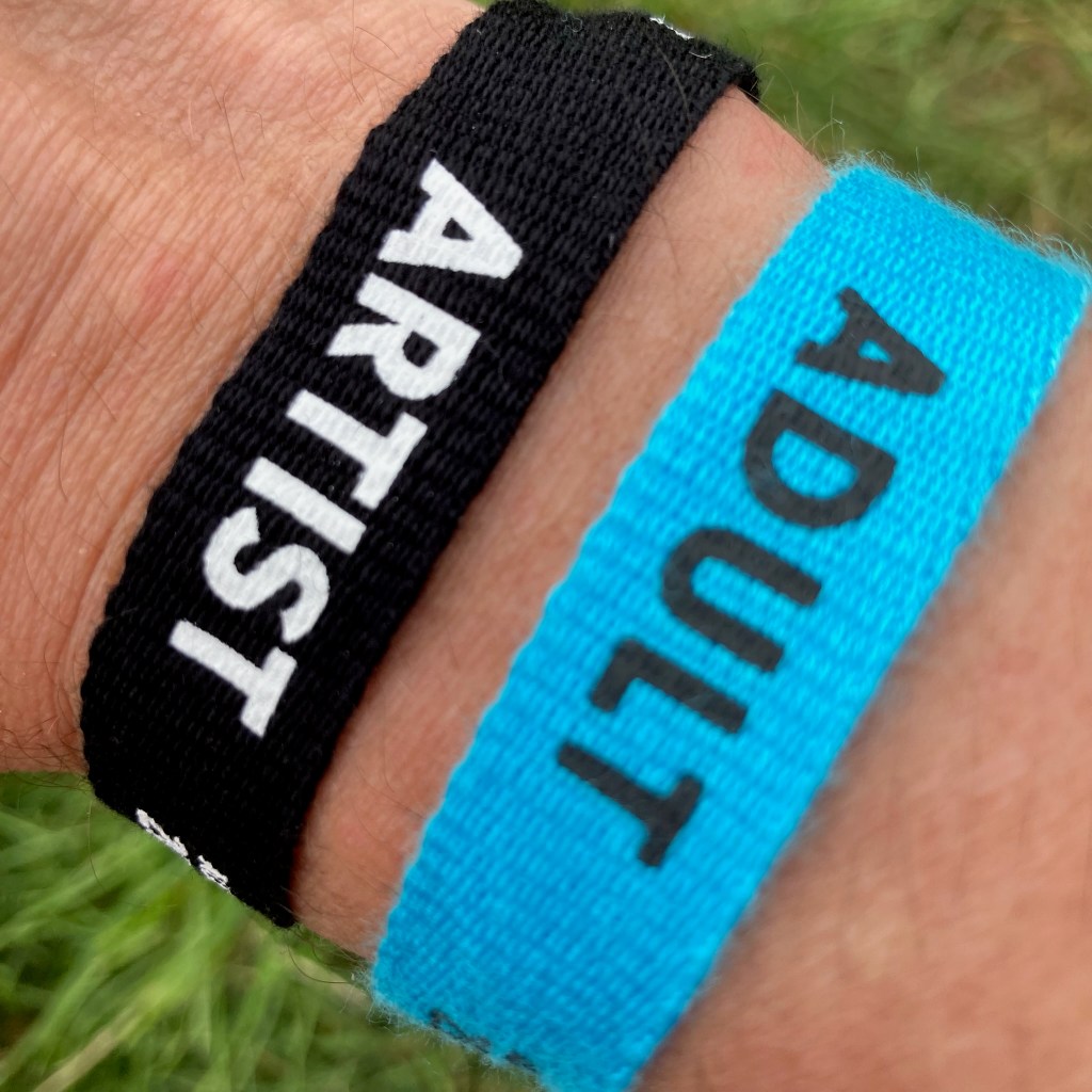 Two festival wristbands on a wrist, one saying Adult, the other Artist.