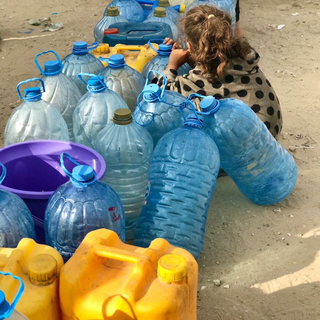 A small girl crouching beside empty plastic water bottles in Gaza.